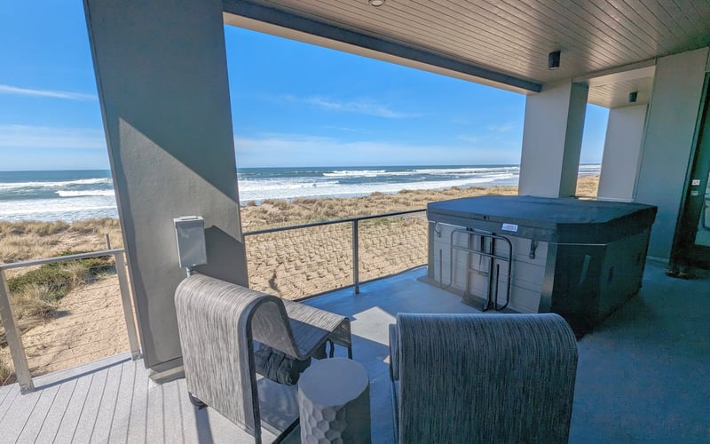 Covered oceanfront deck with seating, grill, and views of beach, dunes, and waves