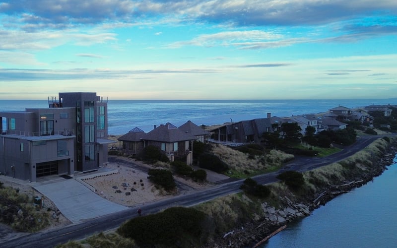 Modern beachfront homes on coastal bluff overlooking ocean and lagoon under blue sky