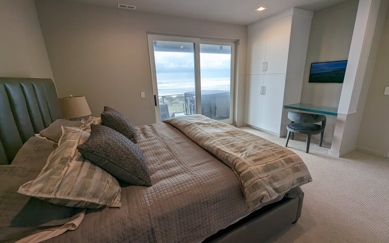 Master bedroom with king bed, green upholstered headboard, and glass doors opening to ocean and mountain views