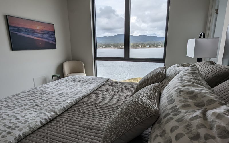 Bedroom with two beds, large windows overlooking lake and mountains, sunset artwork on wall