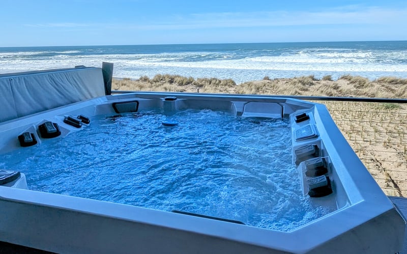 Blue hot tub on beach deck overlooking ocean waves and dune grass