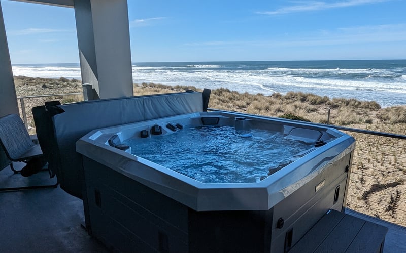 Hot tub on covered oceanfront deck with beach and waves visible beyond dune grasses