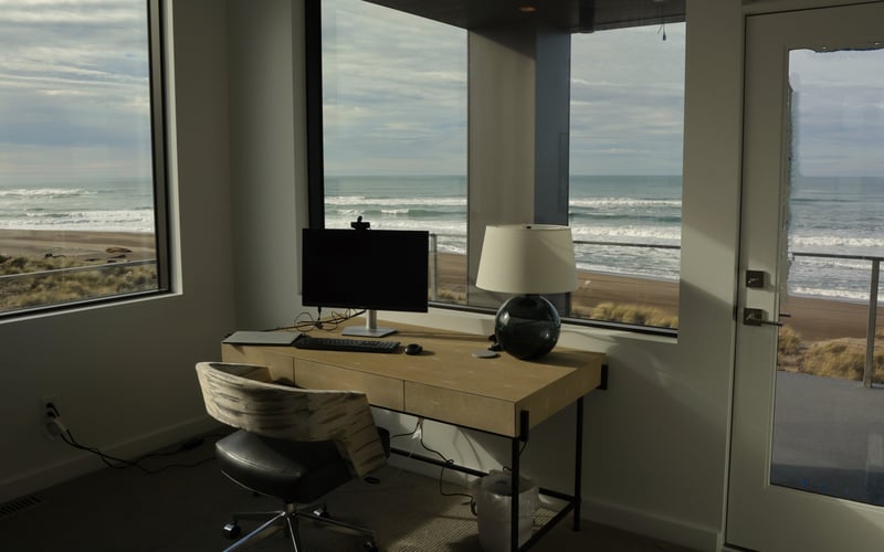 Beachfront desk with computer monitor and lamp overlooking ocean waves and sandy beach